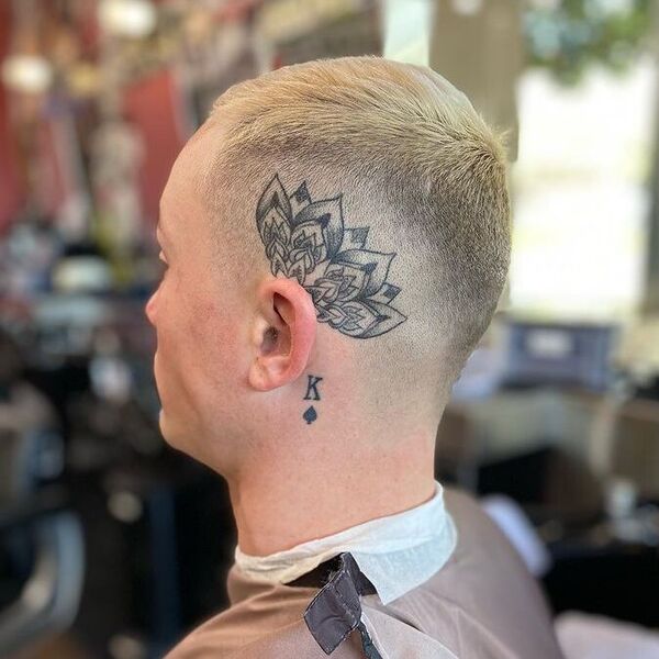 Blonde Mohawk with Tattooed Fade - a man wearing a barber cape.