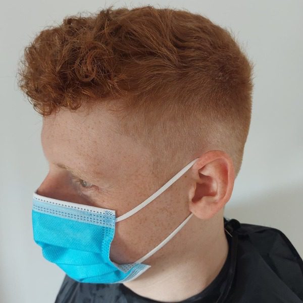 Curled Caramel Top with Undercut - a man wearing a mask and barber cape.