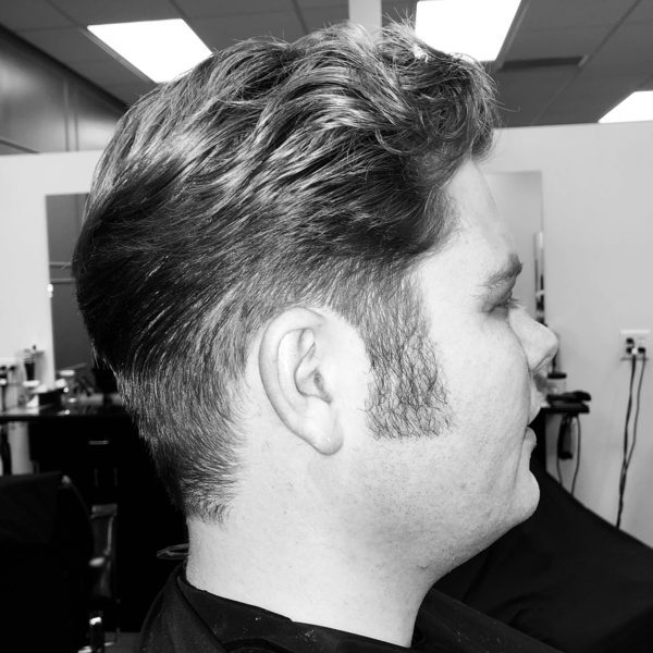 Curly Faded Ducktail Haircut - a man wearing a black barber cape.