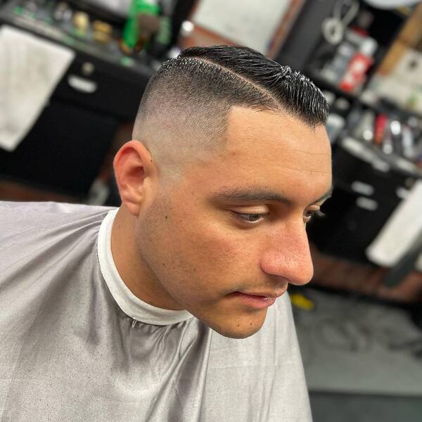 Clean Cut Comb Over Fade- a man wearing a silver barber's cape