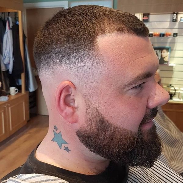 Low Skin Fade Crew Cut with Beards - a man wearing black shirt with stripe barber cape.
