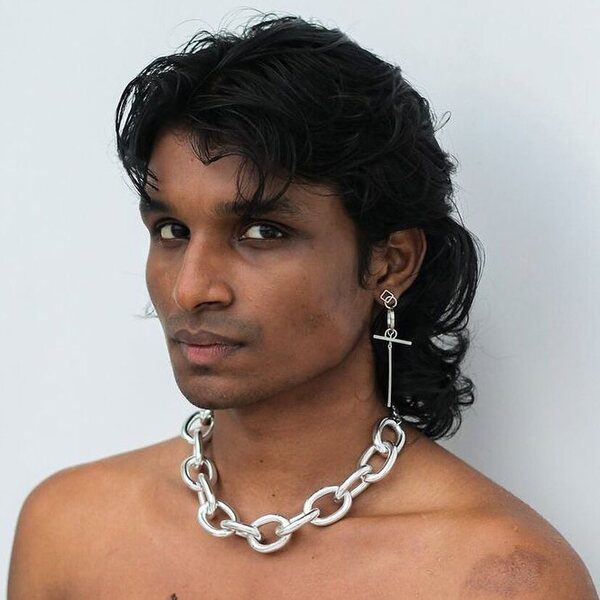 A man wearing a thick chain necklace and a cross sign design earring